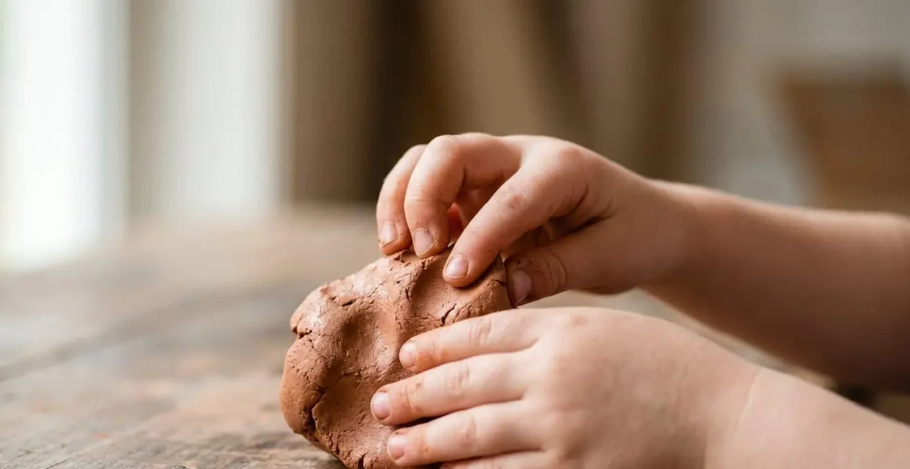Gros plan sur les mains d'un enfant modelant de la pâte, symbolisant l'expression et la transformation émotionnelle